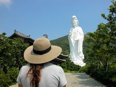 a woman wearing a hat standing in front of a white statue with a buddha behind her