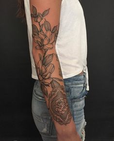 a woman's arm with flowers and leaves tattooed on her arm, in front of a black background