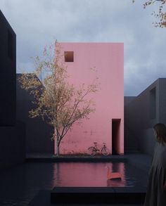 a woman standing in front of a pink building with a bike parked next to it