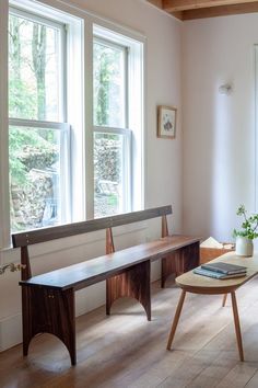 a room with two windows and a bench in the corner next to a table that has a potted plant on it