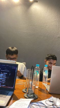 three boys sitting at a table with laptops