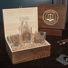 an empty glass bottle and three glasses in a wooden box on a table next to cigars