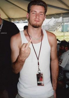 a man in white tank top holding up a peace sign and wearing a necklace with an american flag on it