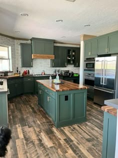 a kitchen with green cabinets and wood flooring is pictured in this image, while a black dog stands near the island