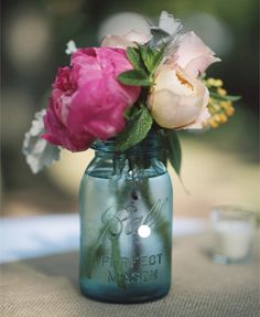 pink and white flowers are in a mason jar on a tablecloth with a glass of water