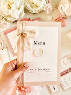 a person holding up a wedding menu on top of a table with flowers and cards