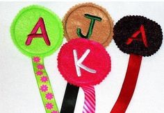 three different colored hair clips with the letters k and j on them, all decorated to look like flowers