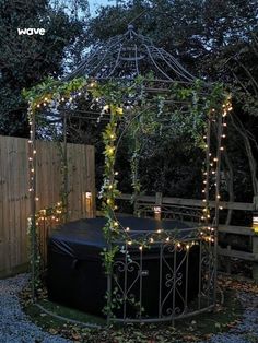 an outdoor gazebo with lights on it and a black tub in the middle surrounded by trees