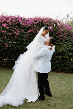 the bride and groom are standing in front of some bushes with pink flowers on it