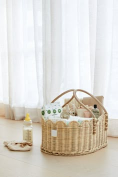 a wicker basket sitting on the floor next to a bottle and baby products in front of a window