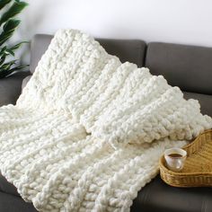 a white blanket sitting on top of a couch next to a basket with a cup of coffee