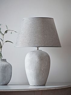 two white vases sitting next to each other on a table with a lamp in front of them