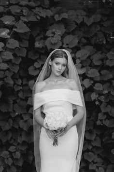 a woman in a wedding dress standing next to a wall covered with leaves and flowers