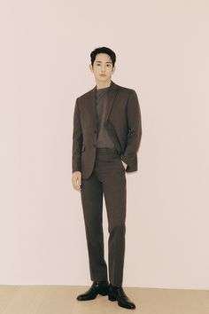 a man standing in front of a white wall wearing a brown suit and black shoes