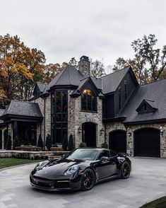 a black sports car is parked in front of a large house with two garages