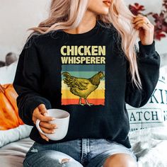 a woman sitting on a bed holding a coffee cup and wearing a chicken whisper shirt