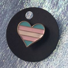 a pink and blue heart pin sitting on top of a black circle