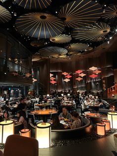 people are sitting at tables in a restaurant with lights hanging from the ceiling above them