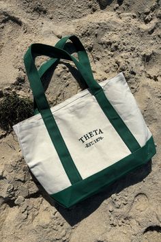 a white and green tote bag sitting in the sand