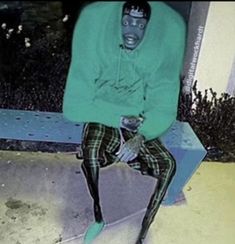 a man sitting on top of a blue bench wearing a green sweater and plaid pants