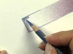 a person is holding a pencil and drawing something on paper with watercolors in their hands