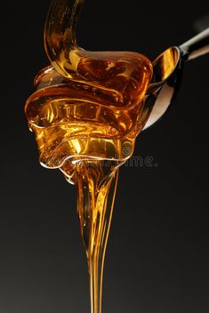 honey pouring from a spoon into a glass bowl with liquid flowing out of it to the side