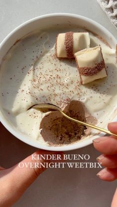 a person is spooning into a bowl of pudding with cream and cinnamon on top