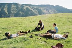 three people sitting in the grass on top of a hill