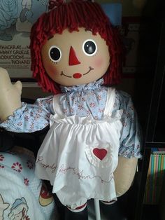 a ragged doll with red hair and big eyes sitting on top of a bed next to a book shelf