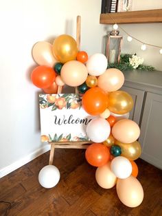 a welcome sign surrounded by balloons on the floor in a room with wooden floors and white walls