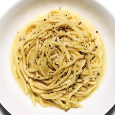 a white plate topped with pasta covered in cheese and seasoning next to a fork