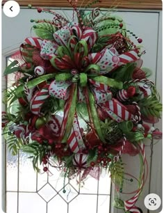 a christmas wreath hanging from the front door with candy canes and bows on it