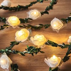 some white roses and green leaves on a wooden table with lights in the shape of flowers