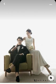 a man and woman sitting on a couch in front of a white wall wearing formal attire