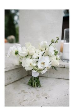 a bouquet of white flowers sitting on top of a stone bench next to a candle