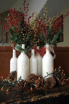 three white bottles with pine cones and red berries in them are sitting on a mantel