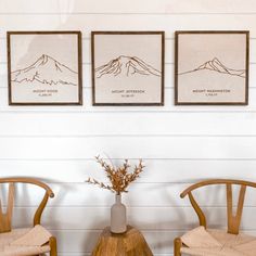 two wooden chairs sitting next to each other in front of a wall with three pictures on it