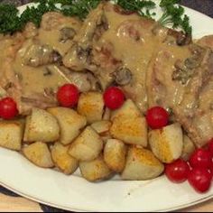 a white plate topped with meat covered in gravy and potatoes next to cherry tomatoes