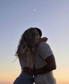 a man and woman standing next to each other in front of the sky at sunset