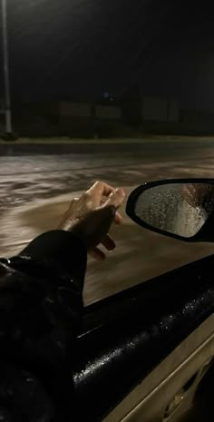 a person's hand on the side mirror of a car at night with rain