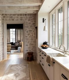 a kitchen with stone walls and wooden floors, along with an open door leading to the outside