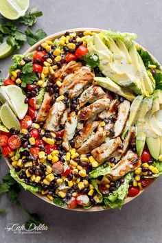 a salad with chicken, avocado, black beans, corn and lime wedges