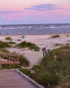 there is a bike parked on the beach next to the boardwalk and stairs that lead down to the beach