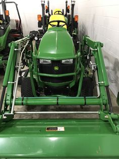 a green tractor parked in a garage next to other tractors