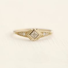 a yellow gold ring with a princess cut diamond set in the center, on a white background