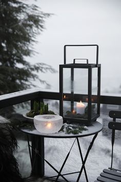 two lit candles sitting on top of a table next to a glass container filled with plants