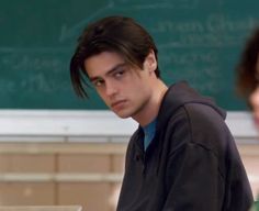 a young man sitting in front of a blackboard while looking at his laptop computer