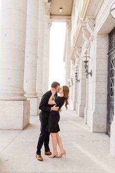 a man and woman kissing in front of an old building with columns on either side