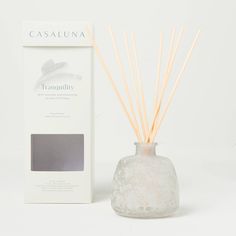 a white vase with some sticks in it next to a box and an empty candle