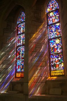 two stained glass windows in a church with the sunlight shining through them and casting long shadows on the wall